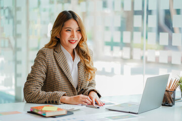 An Asian female accountant sits at a desk with a laptop and calculates financial graphs showing investment results. Plan a successful business growth process in the office.