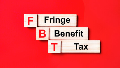 On a bright red background, wooden cubes and blocks with the text FBT Fringe Benefit Tax. Manufacturing of wooden toys.