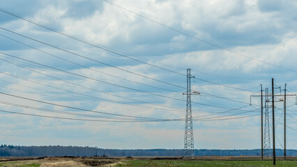 High voltage post on blue sky with clouds background. Electrical net of poles on blue sky and spring meadow.