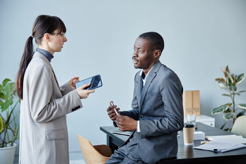 Minimal side view portrait of young businesswoman talking to African American mentor against light...