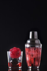 Red cocktail with ice in a glass and a shaker on a black background. Summer cold alcoholic soft drinks, drinks and cocktails.