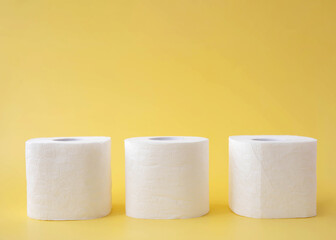 On a yellow background there are three rolls of toilet paper a place for text