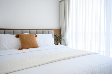 Modern interior cozy bed near a window with white curtains in bedroom. pillows and white soft blanket for rest and sleep.