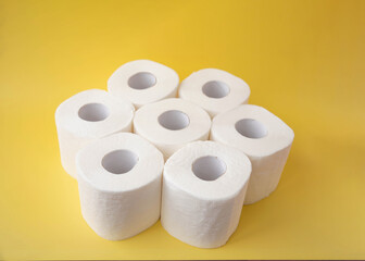 On a yellow background, seven rolls of toilet paper stand side by side