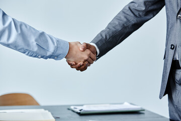 Side view close up of two business people shaking hands at meeting against simple blue background,...