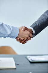 Vertical close up of two business people shaking hands at meeting against simple blue background