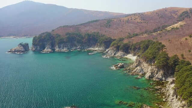 A beautiful rocky island and a cape in a beautiful bay covered with coniferous trees. Sea waves crash on the shore. Beautiful rocks are covered with pine trees. The concept of outdoor recreation