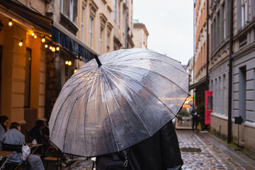 Close up big transparent umbrella under the rain. Europe travel, evening walk, rainy weather. Male under an umbrella with raindrops.
