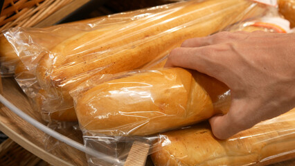 Close-up of beautiful packaged baguettes on a wooden counter and a male hand takes one