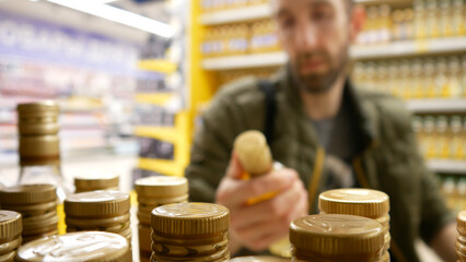 Close-up of many olive oil bottles on a store shelf and a man reads the composition holding one bottle