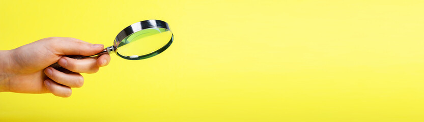 Banner with hand holding magnifier on yellow background. Thorough information search and learning,...