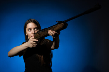 a young girl with long flowing hair in a black T-shirt aims a gun on a dark background