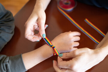 Woman putting a LGBT rainbow bracelet on a young girl's wrist