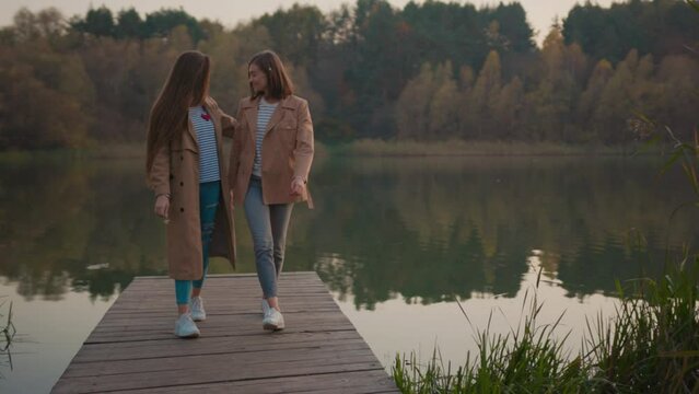 Couple of beautiful young romantic woman walking on lake shore in picturesque autumn landscape. Lovable girlfriends smiling enjoying pleasant date outdoors.