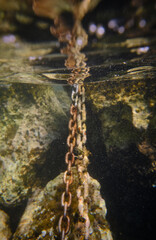 Old chain near stones in clean water in sea