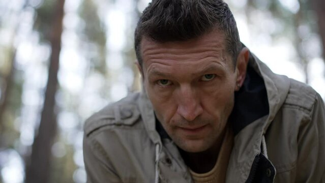 Close-up portrait of exhausted male survivor standing in forest looking at camera. Tired Caucasian adult confident man posing in wood with serious facial expression. Trips and adventures