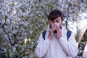 Man with nose wiper near blooming tree rhinitis suffering from seasonal allergy symptoms of cold
