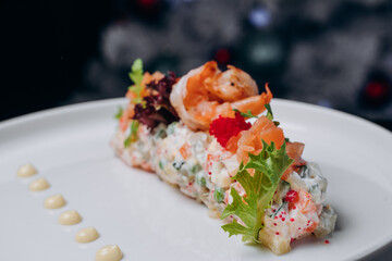 Olivier salad in a white plate in a festive atmosphere. A traditional Russian dish for Christmas and New Year