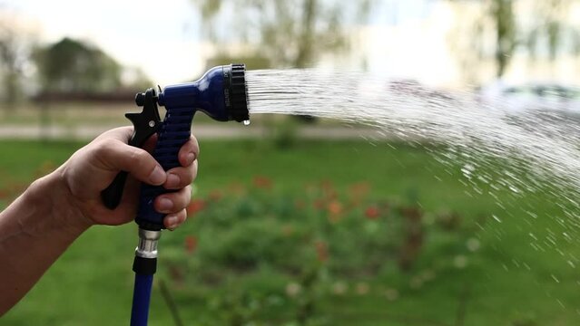 close up male hand holding water hose and watering lawn or plants on backyard. gardener man with sprinkler in garden. hobby concept