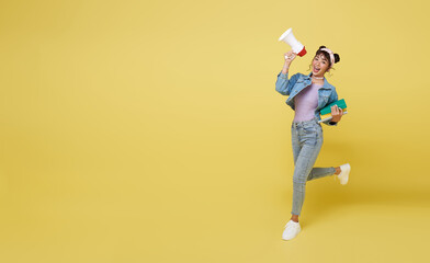 Happy Asian girl holding a book and jumping shouting at an announcement megaphone on a yellow...