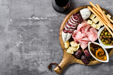 Italian snack and antipasti on a tray and red wine: prosciutto, salami, sun-dried tomatoes, olives,...