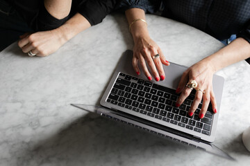 Cropped hands and arms of two women collaborating and working on a laptop on a marble table