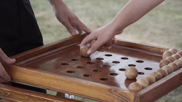 Man hand removes balls from field of wooden game of nim. Woman takes balls from board with holes. Winning move, game over. Famous Chinese entertainment for development of ingenuity and intelligence.
