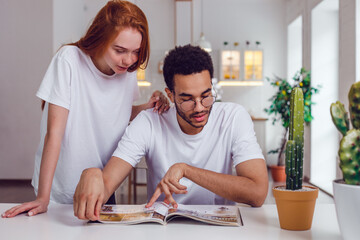 The couple reading a magazine together at the table. African American guy and red-haired girl.