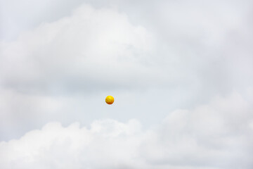 Yellow softball in the air with clouds and sky in background. With copy space.