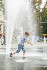 Happy little boy playing in square between jets of water in dry fountain on summer day. Having fun