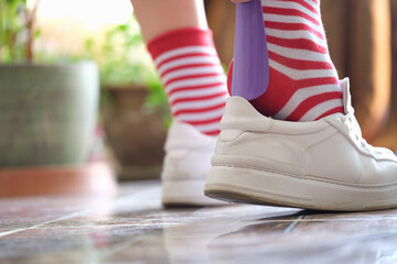 Person puts shoes white sneakers using shoehorn