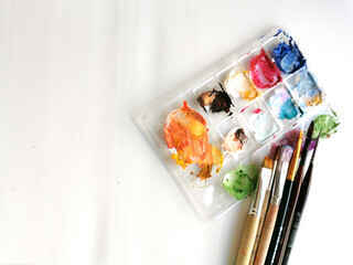 Palette with samples of multi-colored gouache paints and brushes after painting. Close-up on a...