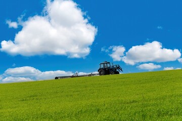 Fototapeta na wymiar The tractor plows the large field against blue cloudy sky background in spring season