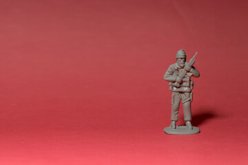 Miniature toy soldier with weapon in hand. Red background.