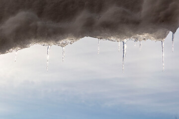 melting icicles with the blue sky and sun in the background. Spring weather with thawing ice