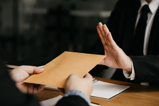 Business Man Raised Her Hand To Deny Accepting A Bribe From A Business Partner, A Brown Envelope Containing A Large Number Of Dollar Bills As Money For Bribery, A Corruption Concept.