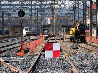 Train track under construction with a red and white sign preventing traffic and a safety pole connecting the catenary to the ground and an excavator machine