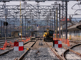 Train tracks under construction with red and white signs preventing traffic and a safety pole connecting the catenary to the ground and an excavator machine