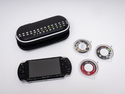 Sony's famous PSP (Playstation Portable) video game console in black on a white background along with three game discs (UMD) and a space invaders case