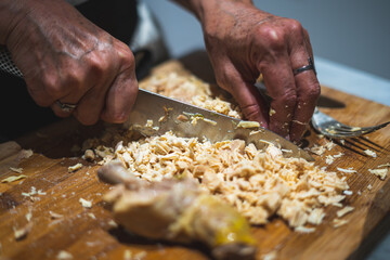 Old woman's hands cutting chicken meat into small pieces