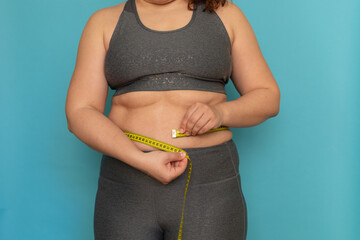 Unrecognizable fat plump overweight woman standing in grey sports bra, leggings, showing excess...
