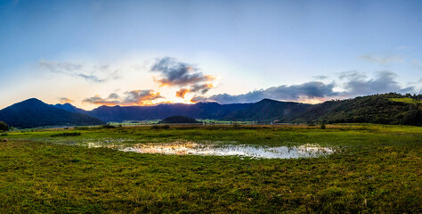 panoramic of volcano crater in the sunset with lake in first plane and mountains in the background, green grass and blue sky in tepetiltic nayarit 