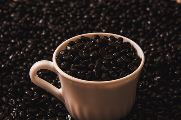 Coffee cup filled with coffee beans on coffee bean surface. Copy space. Selective focus.
