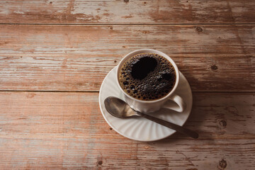 Coffee cup with saucer and spoon on vintage wood surface. Copy space. Selective focus.