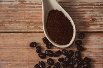 Spoon with ground coffee and coffee beans on vintage wooden surface. Copy space. Selective focus.