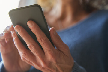 Hands with wrinkles of senior woman texting with smartphone