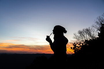 Silhouette of a woman drinking yerba mate at sunset