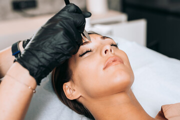 Cosmetologist measures the proportions of the eyebrows with the ruler. Micropigmentation work flow in a beauty salon.