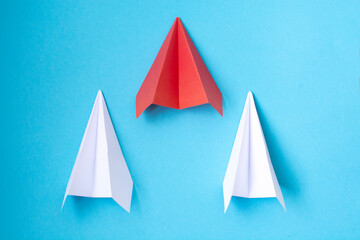 a red paper airplane and two white ones on a blue background. The concept of leadership, teamwork and courage.