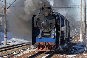 Tourist retro steam locomotive riding on a railroad in a puff of smoke